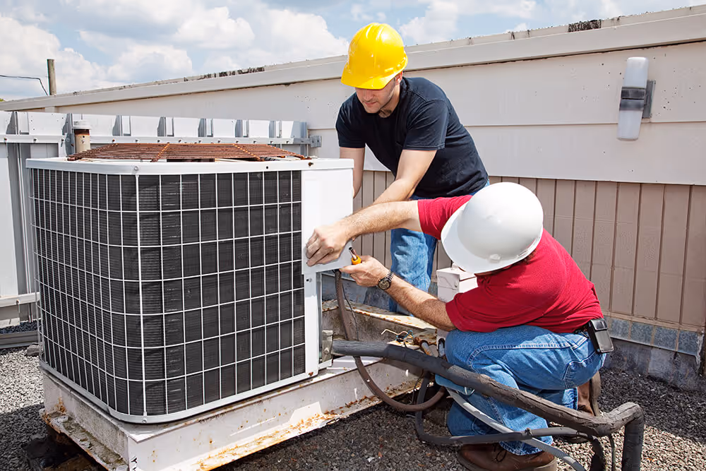 Photo of two repairpeople working on an AC unit on a roof